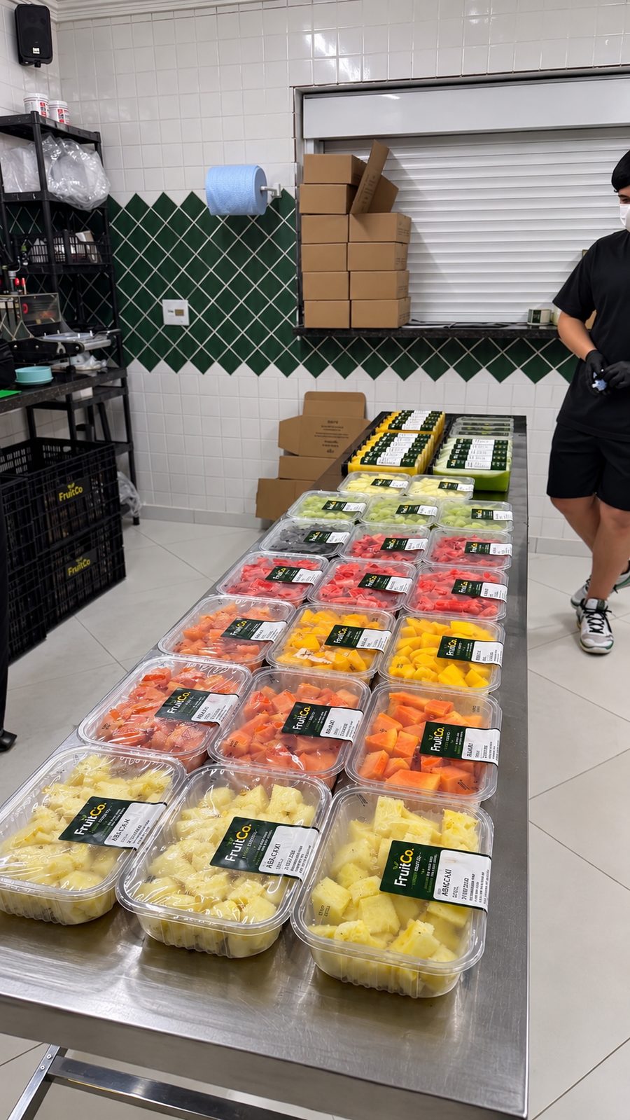 Bandejas de abacaxi, mamão, melancia, manga e melão etiquetadas na bancada de inox da FruitCo